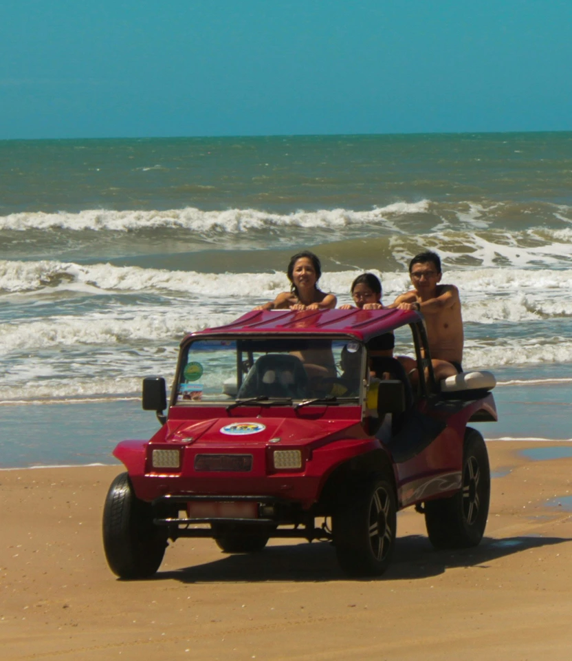 Turistas curtindo passeio em buggy vermelho na beira do mar em Florianópolis.