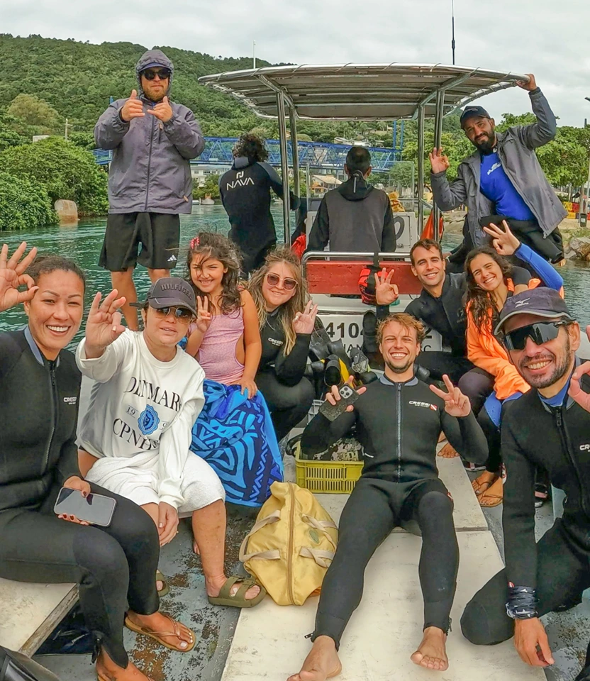 Turistas e instrutores de mergulho sorrindo e comemorando a bordo de embarcação em Florianópolis.
