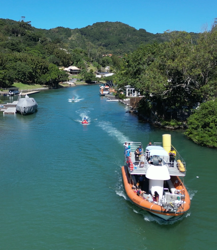 Vista aérea do barco Borrachão navegando em águas calmas cercadas por vegetação em Florianópolis.